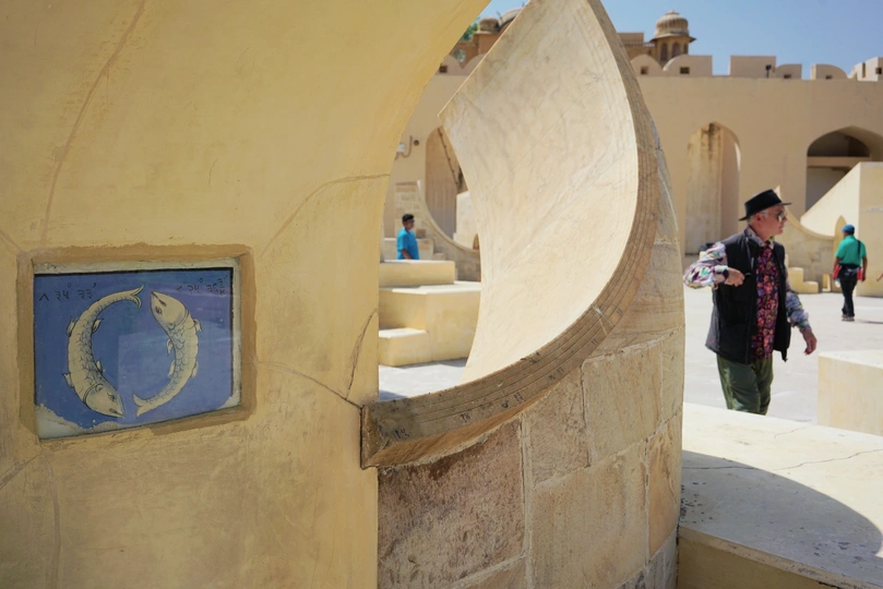 一个人站在一个有拱形建筑的庭院中 周围有人经过。