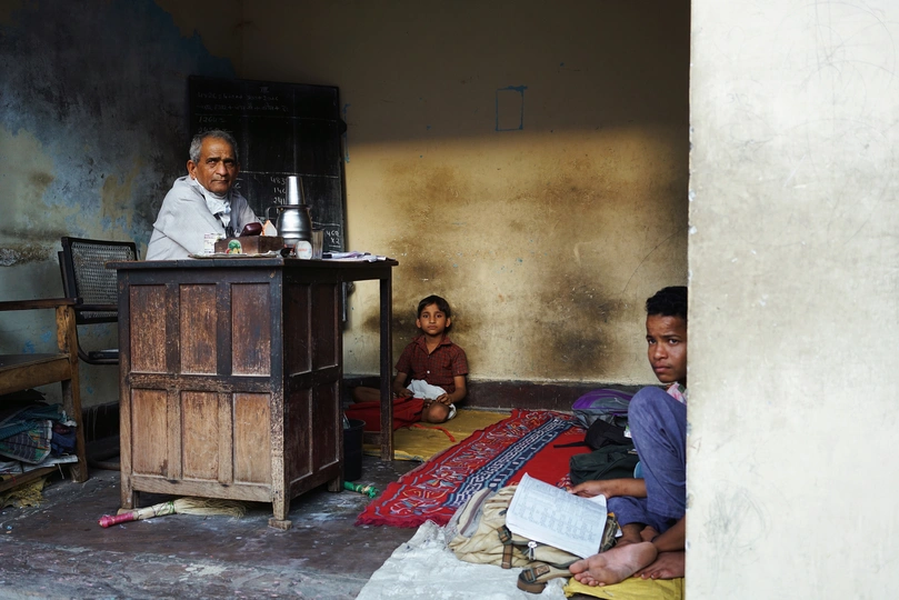 一个男子坐在破旧的客厅里的小桌子旁 一个孩子坐在地板上。