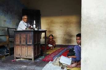 一个男子坐在破旧的客厅里的小桌子旁 一个孩子坐在地板上。