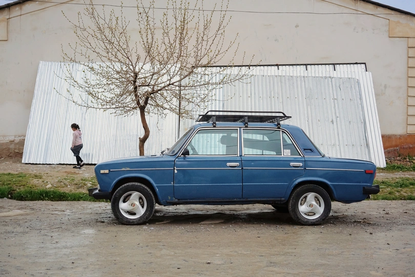 停在建筑物前面的蓝色汽车旁 有一个人经过。