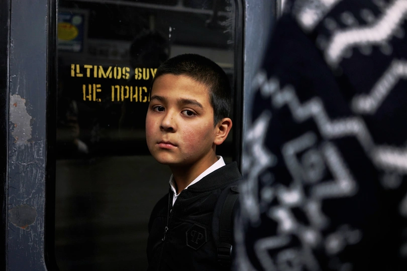 一个小男孩穿着制服 正在火车窗口向外看 另一个孩子站在门口。