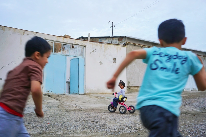一个小男孩在破败的建筑物后面的小街上踢足球 还有一个小男孩骑着三轮车。