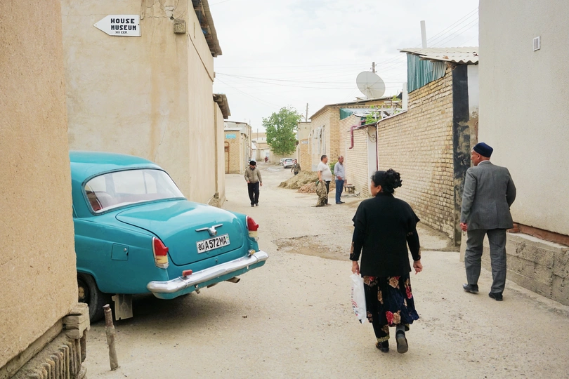 一辆蓝色的汽车停在一条狭窄的巷子里 一名男子骑自行车 一名女子沿着街道走。