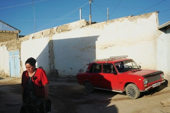 一位女士走过一辆停在白色建筑前的小红车。