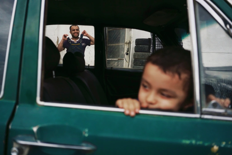 一个年轻的男孩坐在绿色的卡车上 透过窗户看着镜子里的一个男人。