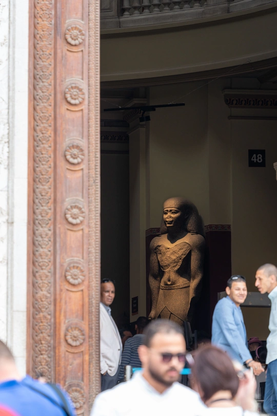 一些人站在一栋建筑外 周围有大型雕像。