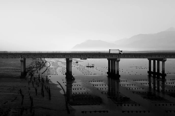 一张黑白照片 火车在水上的一座桥上。