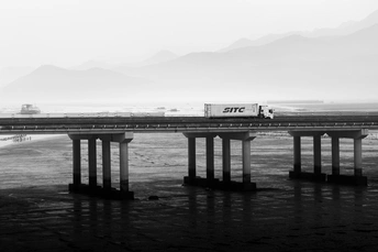 一张黑白照片 展示了一列火车在大型水域上方的桥上行驶。