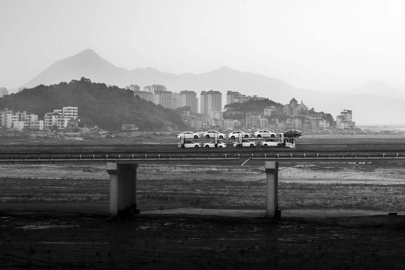 一张黑白照片 背景是一座城市 公路边停着汽车。