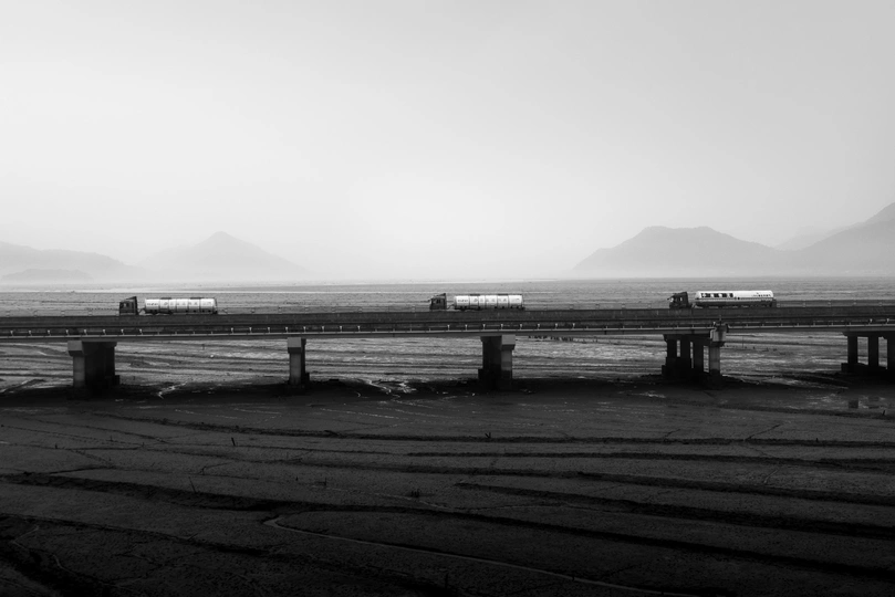 一张黑白照片 展示了一列火车穿越水面上的桥。