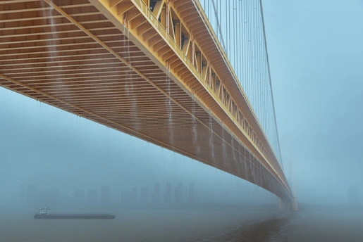 雾蒙蒙的早晨 一座悬索桥上有一艘船在水里。