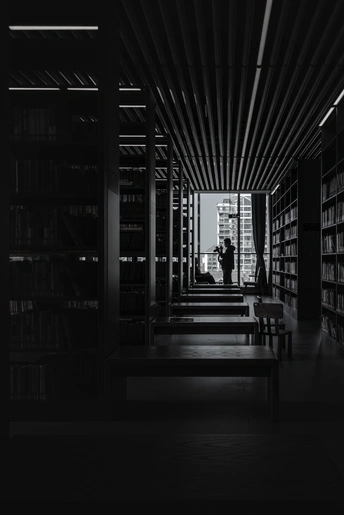 一张黑白照片 展示了一个有书架的黑暗房间 一个人站在长凳上。