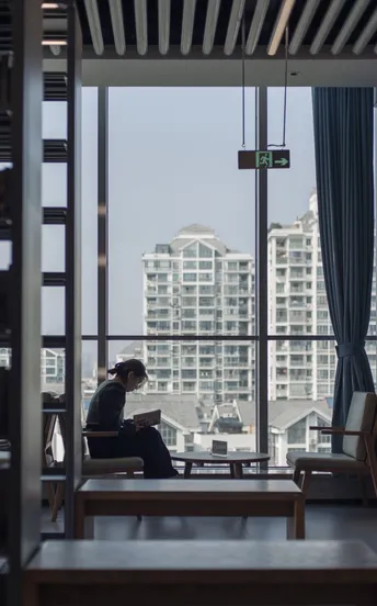 一个人在一个有大窗户的房间里读书 窗外是城市。