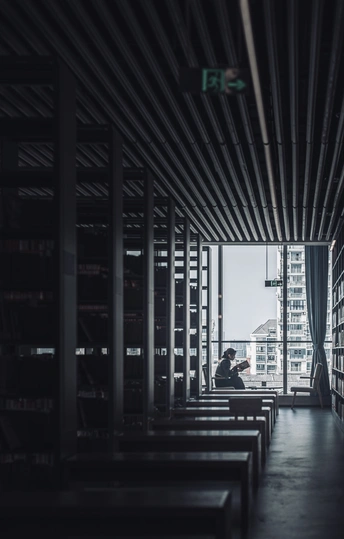 一个光线昏暗的房间 窗外有一个人正在 bench 上阅读一本书。