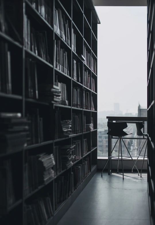 一个充满书架的书房 前面有一张桌子和一把椅子 旁边是一扇大窗户。