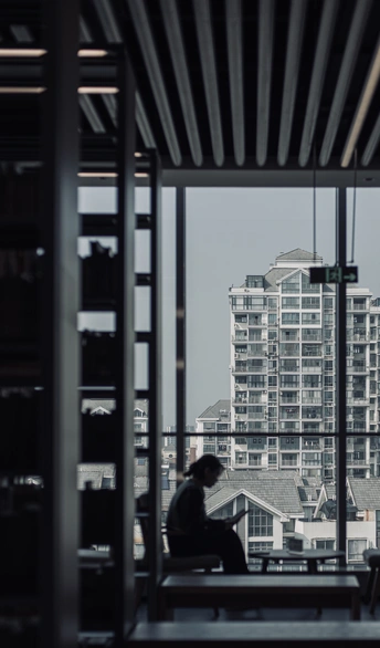 一位女性坐在长凳上 凝视着一座高楼 窗外。