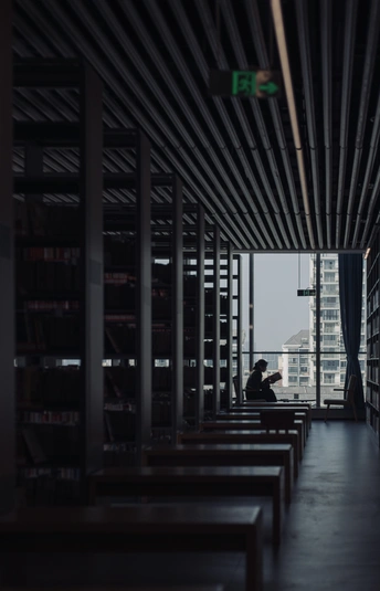 一个光线昏暗的房间 窗外有巨大的窗户 一个人在长凳上读书。