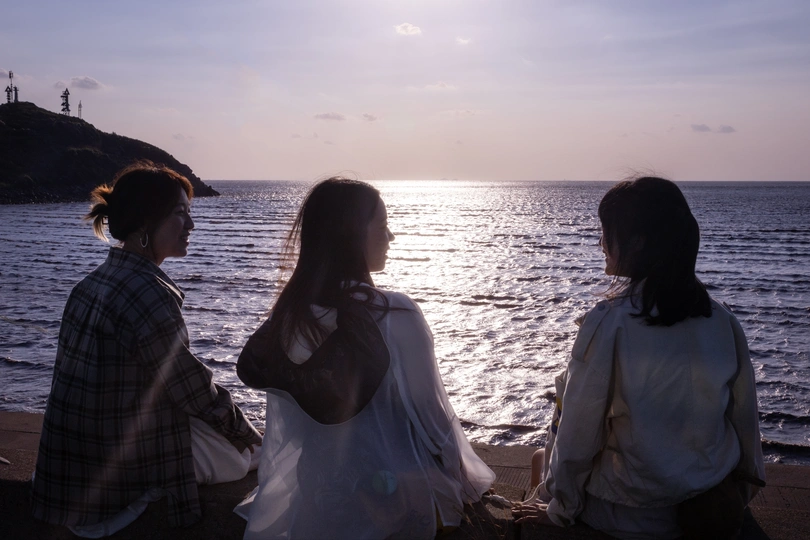 两位年轻女子坐在海滩上 观赏海洋的日落。