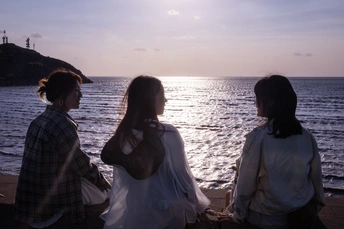 两位年轻女子坐在海滩上 观赏海洋的日落。