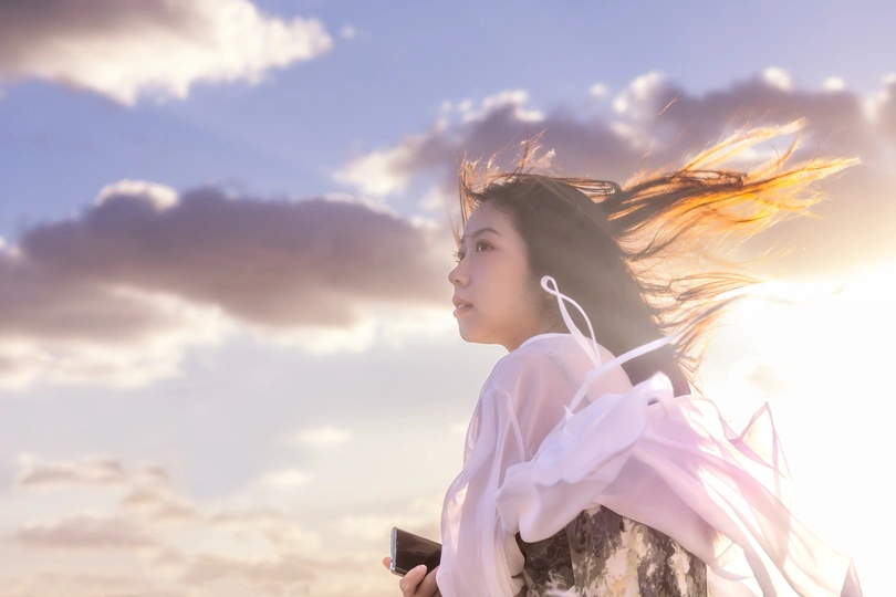 一位美丽的年轻女子穿着一件白色连衣裙站在海滩上 太阳在她的身后 云在风中吹动。