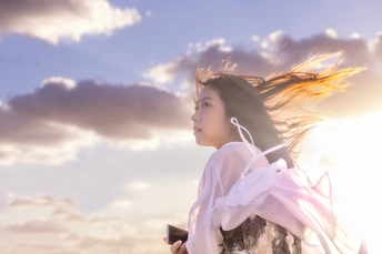 一位美丽的年轻女子穿着一件白色连衣裙站在海滩上 太阳在她的身后 云在风中吹动。