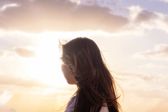 一位年轻女子站在海滩上 望着海洋 此时太阳低垂在天空中。