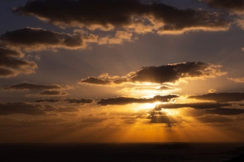 夕阳或日出时 太阳在云层后的多云天空中落下 水体或海洋上空