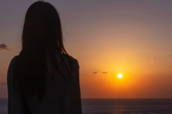 一位年轻女子站在海滩上 观赏着夕阳西下 水面的剪影。