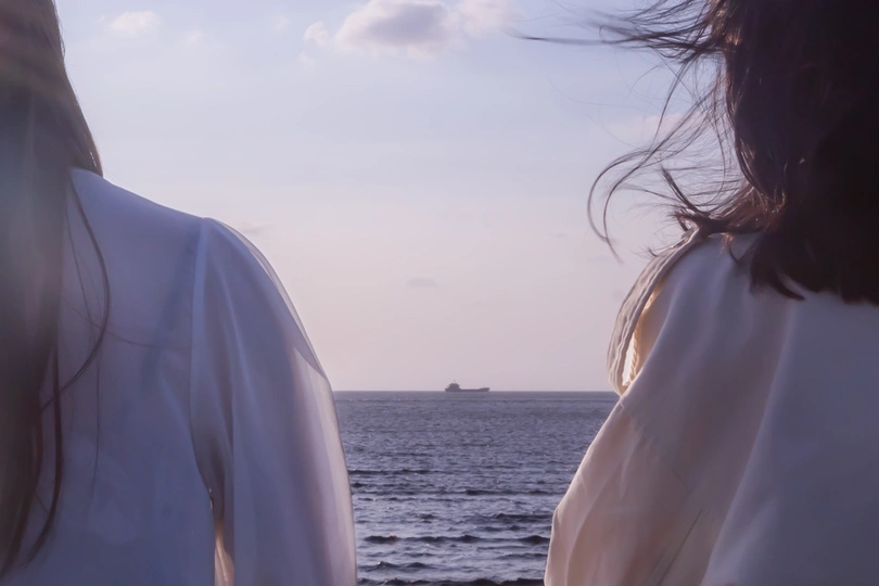 一些穿白衣服的女人站在海滩上 看着夕阳下的海洋。