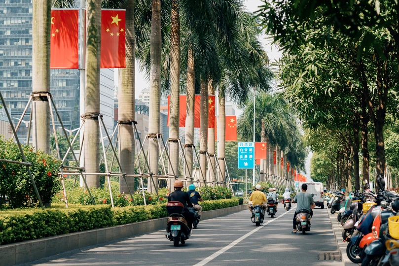 许多人骑摩托车穿过一条树木成荫的街道