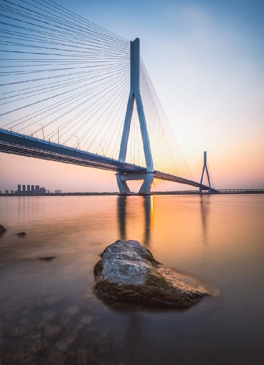 夕阳下 一座横跨在河上的长桥 前景有一块巨大的岩石。