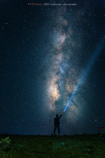 一个人站在夜晚星空下 手持电筒指向星星的剪影。