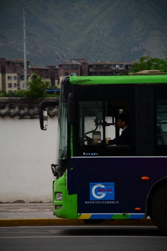 一辆蓝色和绿色的公交车驶过一座建筑物旁边 背景是山脉。