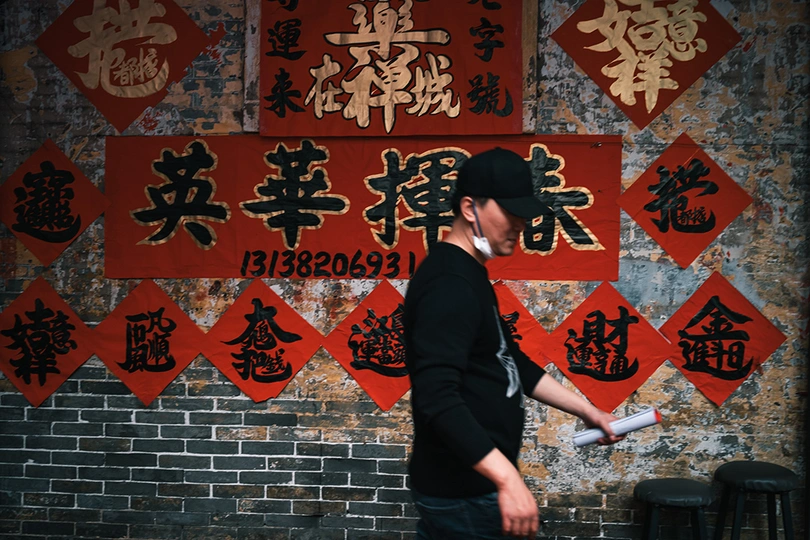 一个戴黑色帽子的人在人行道上骑着滑板车靠近砖墙。