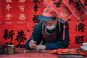 一个在红色雨伞下工作并书写中文书法的男子