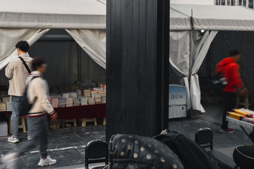 一个穿红衬衫的男人在雨中走过帐篷和椅子