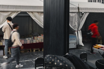 一个穿红衬衫的男人在雨中走过帐篷和椅子