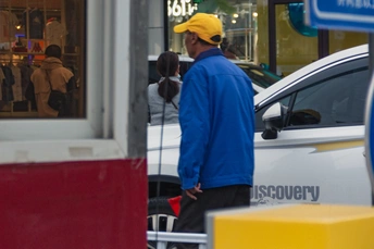 一位穿蓝色衬衫和黄色帽子的人在商店外等待 人们路过。