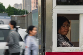 一位老妇人正在红色公共汽车的车窗旁看着经过的人们。