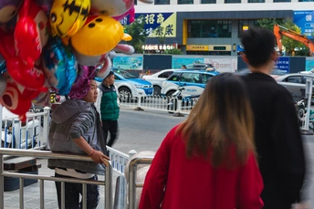 一个人和一个女人走过一个街头小贩推着卖气球的推车。