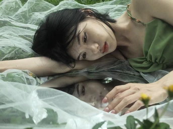 一位穿着绿裙子的年轻女子躺在一片花丛和草地上的一张水床上。