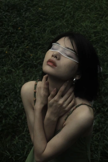 一个戴眼镜的年轻女子躺在草地上 双手捂住脸