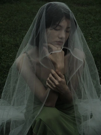 一个穿着婚纱头戴面纱的女孩坐在草地上 双手合十背后