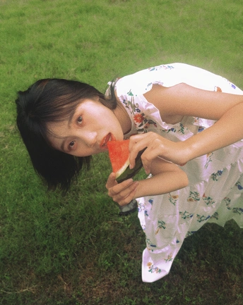 一个穿着连衣裙的年轻女子在草地上拿着一个西瓜。