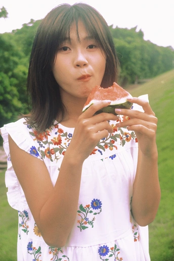 一位穿着连衣裙的年轻女子在公园里吃西瓜。