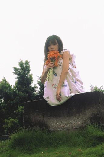 一个小女孩穿着裙子 抱着花 坐在岩石上。