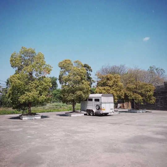 一辆小白色货车或拖车停在靠近一些树的小停车场里。