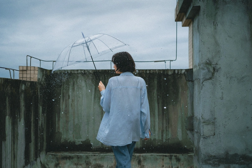 一位穿蓝色雨衣的女人站在雨中 在雨伞下。