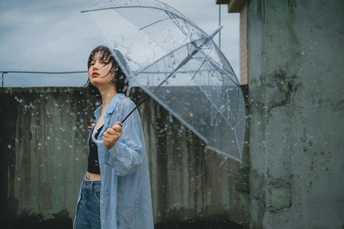 一位穿着蓝色雨衣的年轻女子手持一把透明的伞。
