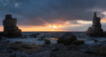 夕阳或日出时一个岩石海滩 水中有岩石堆 太阳低垂在天空中。